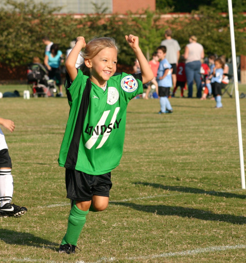 little girl playing soccer, celebrating scoring a goal